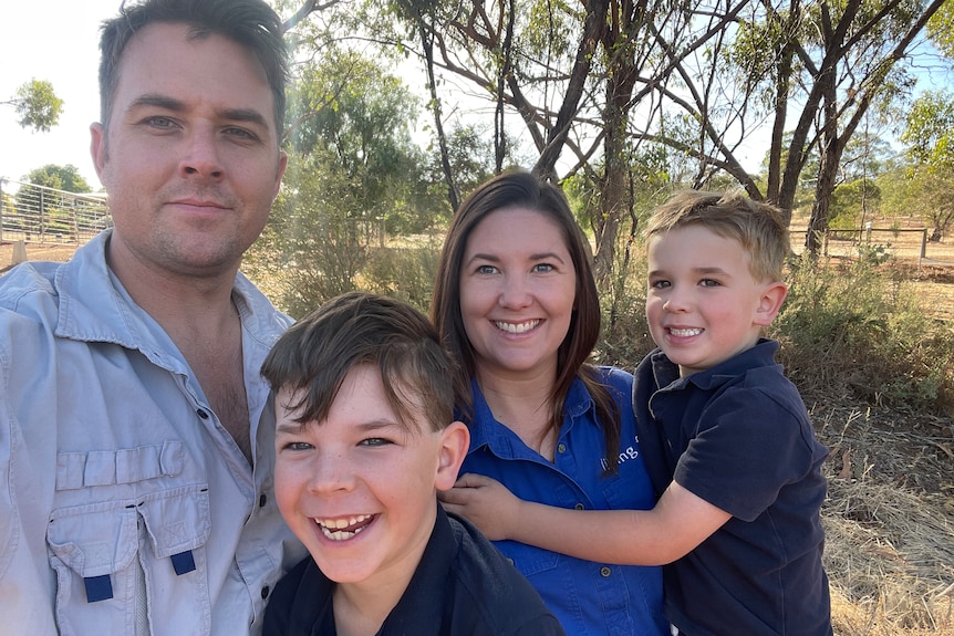 A young family smiling while standing outside near bushland.