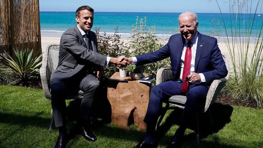 President Joe Biden and French President Emmanuel Macron shake hands while sitting
