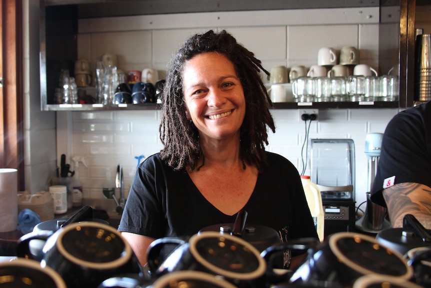A woman in a cafe smiles behind a stack of coffee cups.