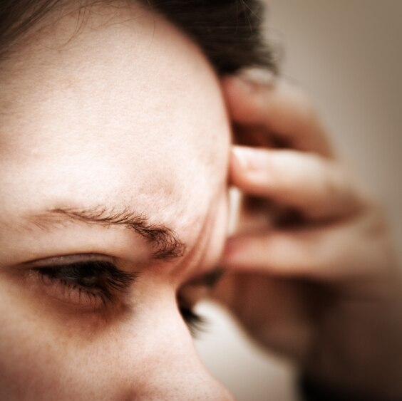 Woman rubbing her forehead winching in pain from a headache.