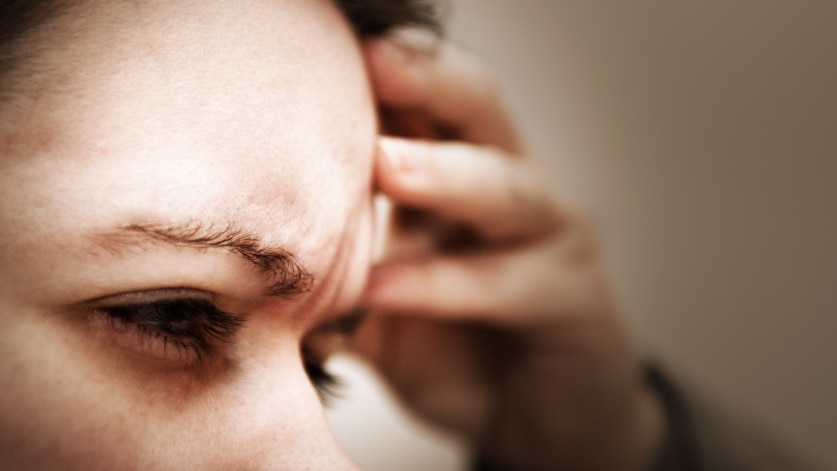 Woman rubbing her forehead winching in pain from a headache.