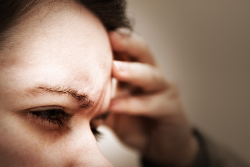 Woman rubbing her forehead winching in pain from a headache.