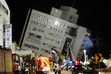 Emergency authorities in front of a multi-storey building, which has tilted.