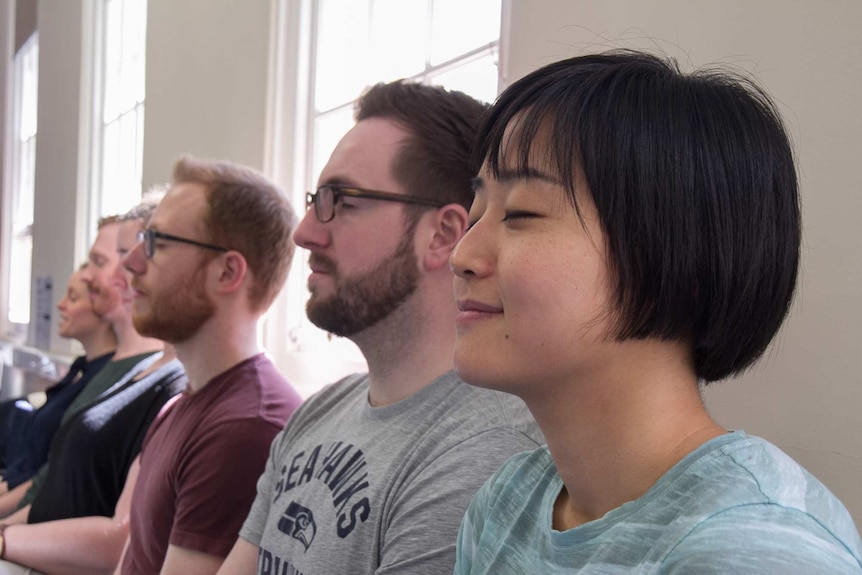 Young people sitting on chairs in a row closing their eyes