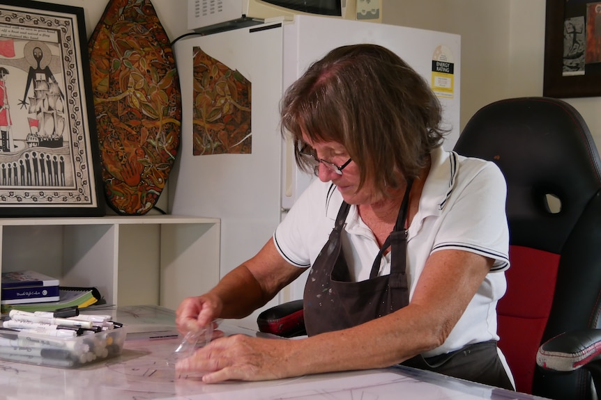 A woman sits at a table, working on artwork. 