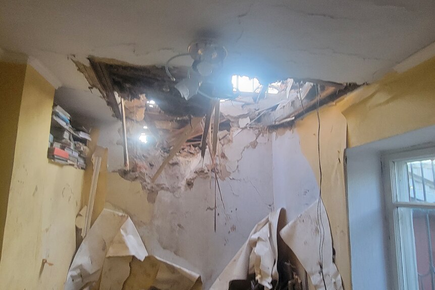 A large area of damage to a ceiling, showing sunlight shining through as wood and plaster hangs down.