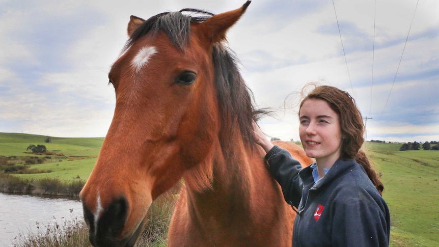 Portrait shot of a woman standing next to a horse on a rural property.