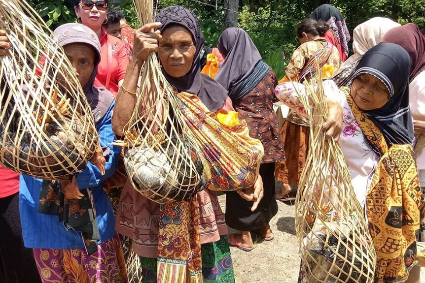 Old women holding poultry inside traditional baskets.
