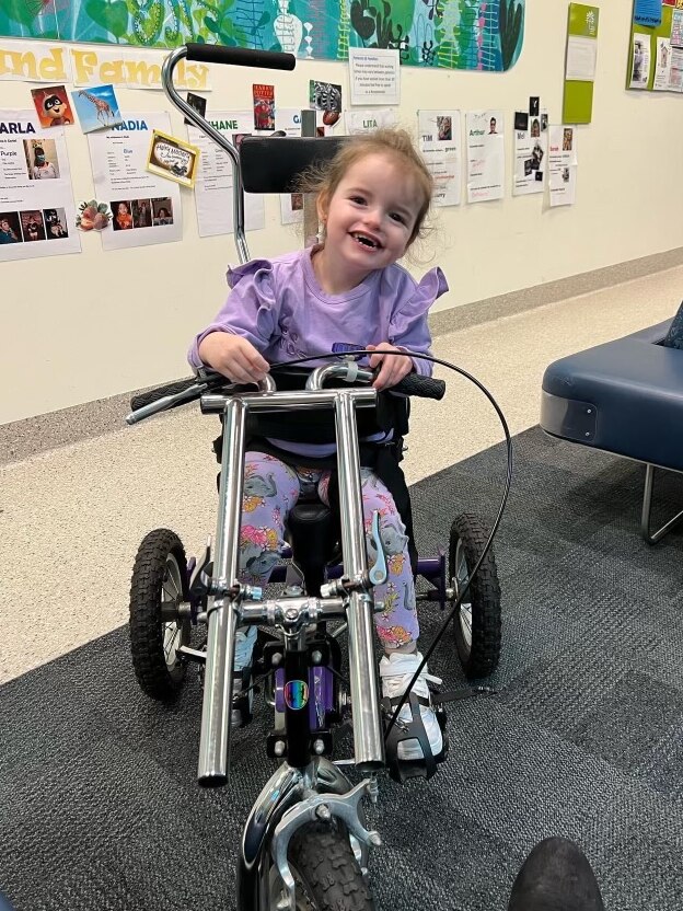 Girl on tricycle at hospital, smiling