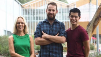 Three smiling people stand in a garden.