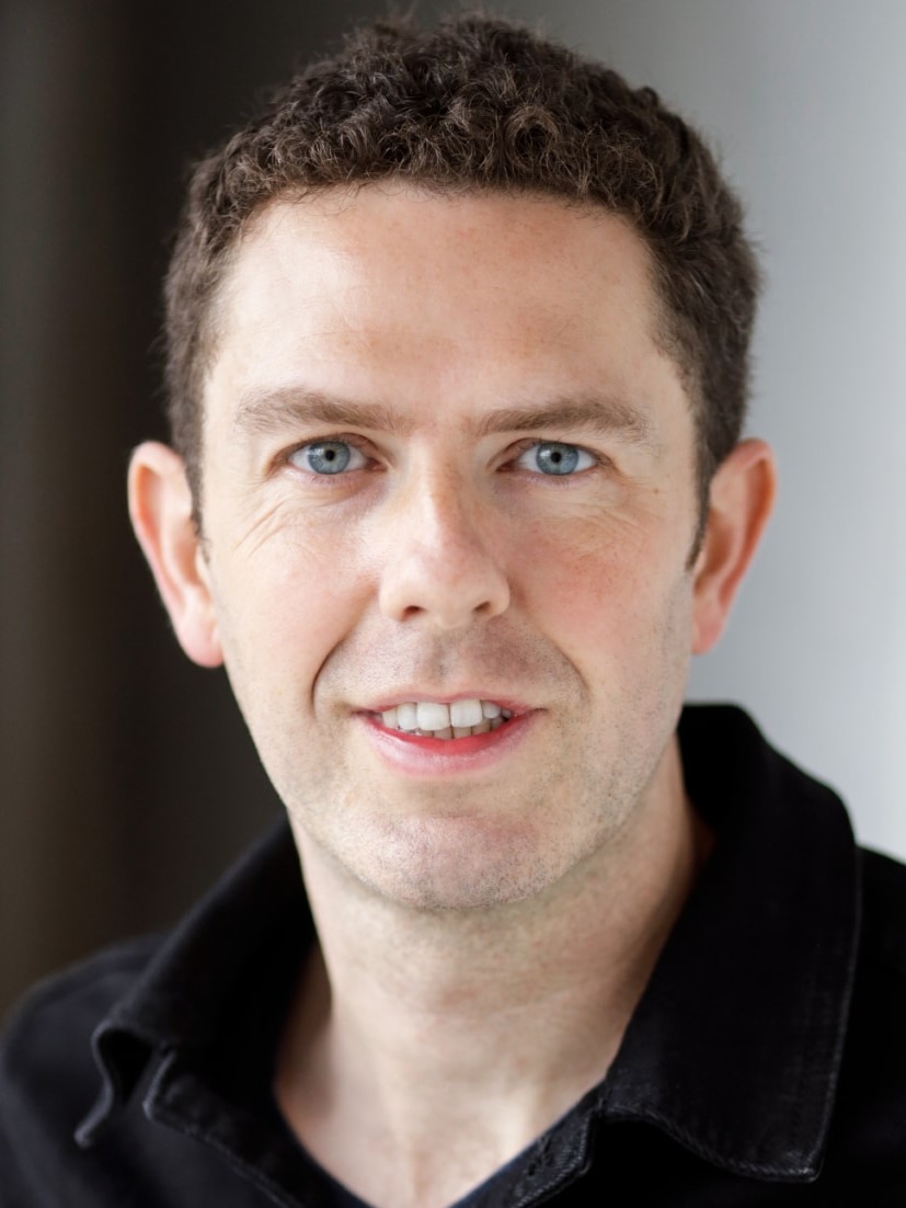 A photo portrait of a man with black hair and a black shirt.