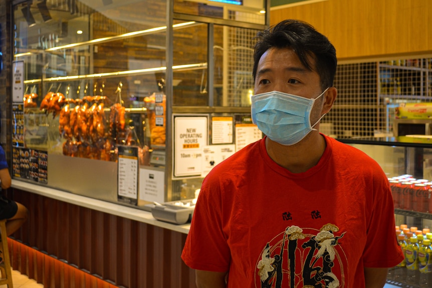 Steven Zheng wearing a surgical mask standing in front of his restaurant with cooked ducks hanging in the window