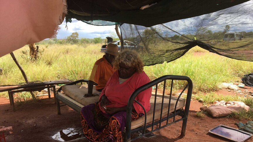 Diane and Mark sit under a tin shelter with hessian sack walls.