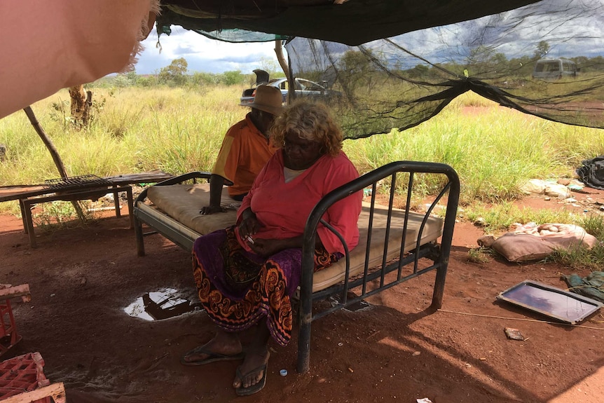 Diane and Mark sit under a tin shelter with hessian sack walls.