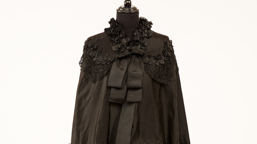 A black cape with  ruffles, lace and a large bow around the neck