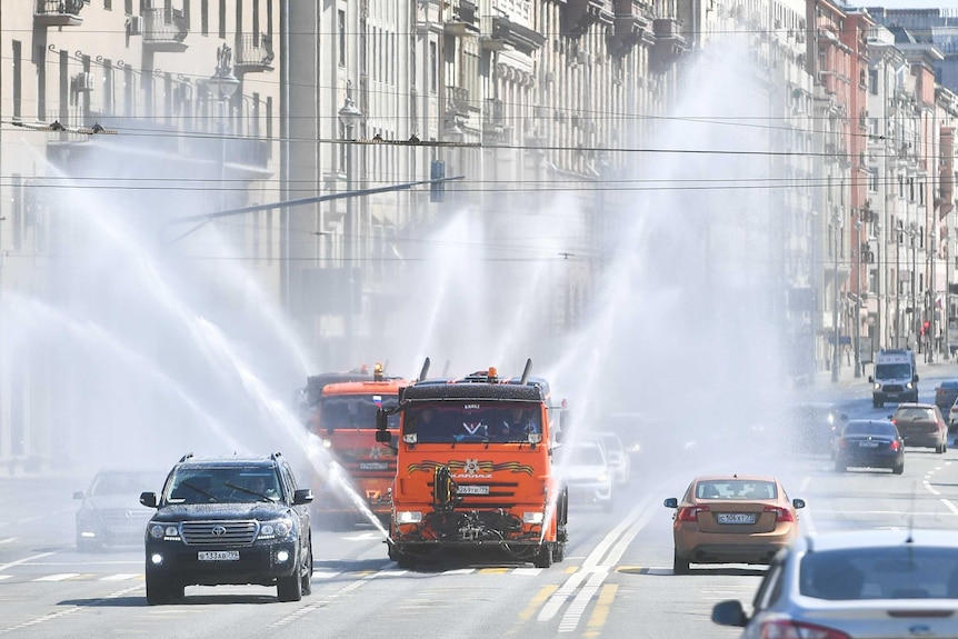two red vehicle sprays liquid into the air as other vehicles drive past