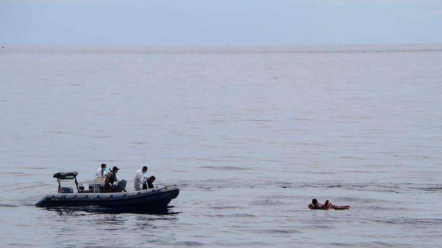 A motor boat with four people abroad approaches a group of people stranded out at sea 