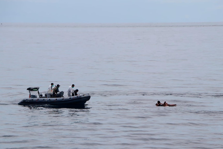 A motor boat with four people abroad approaches a group of people stranded out at sea 