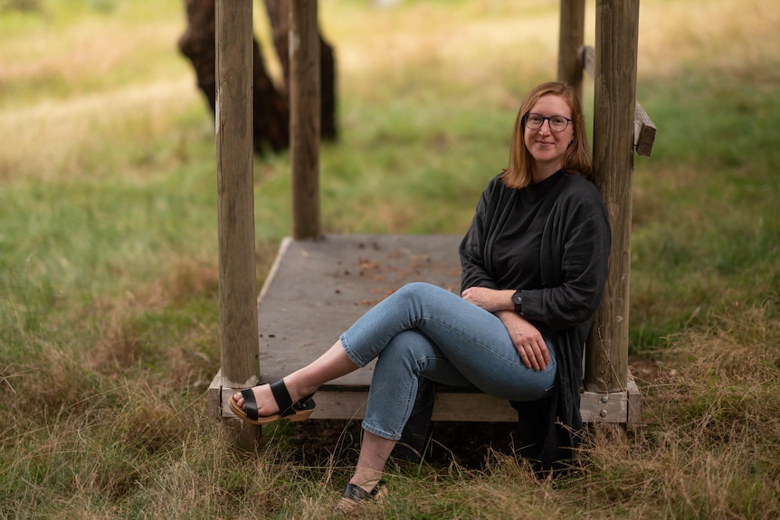 A woman sits in a paddock with one leg over the other