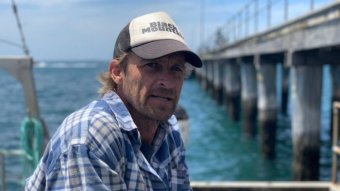 A man in a hat sits near a jetty.