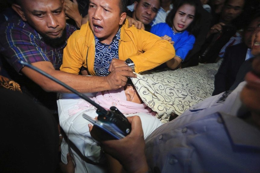 People crowd around a man covered in blankets on a stretcher.