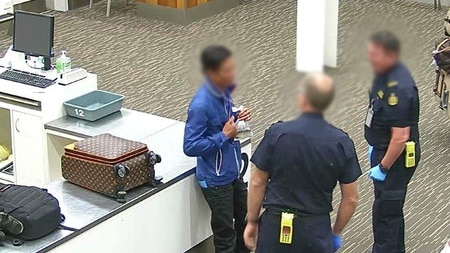 Two uniformed men speak to a third man with a bag of water around his neck