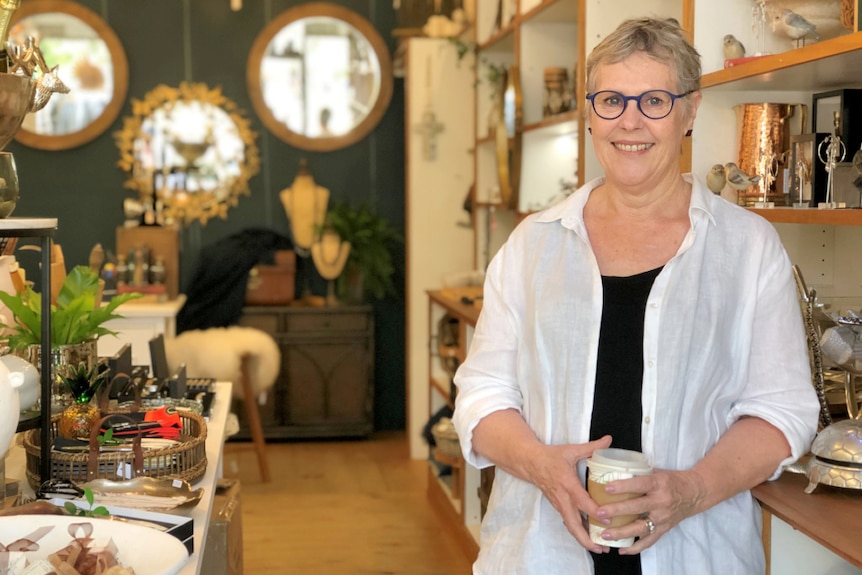 Woman stands holding a take away cup in a shop with a lot of household items.