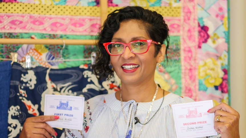 A woman standing in front of homemade items holds up her first and second prize places