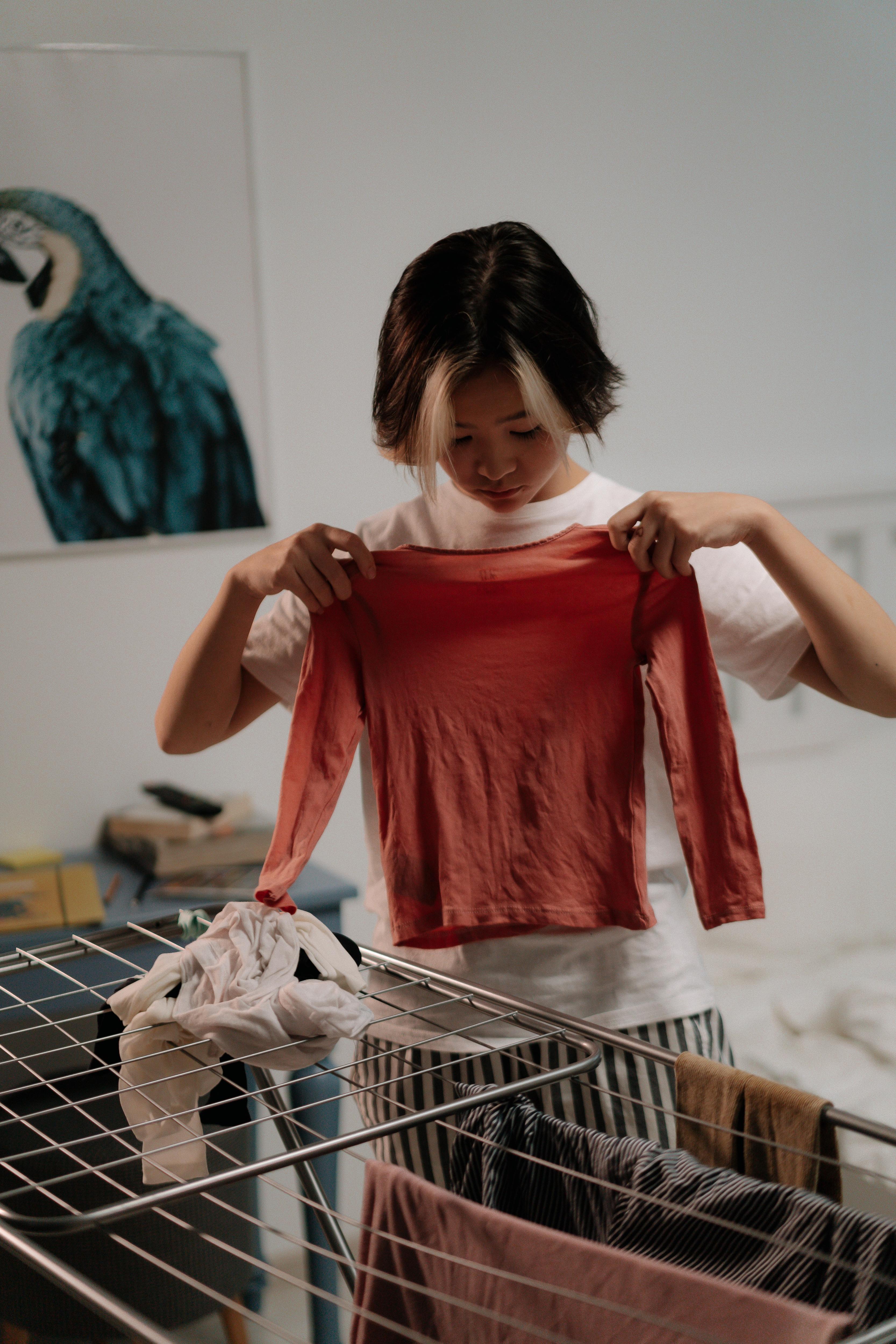 A woman doing her washing holds up a thin, delicate shirt that seems to be too small for her.