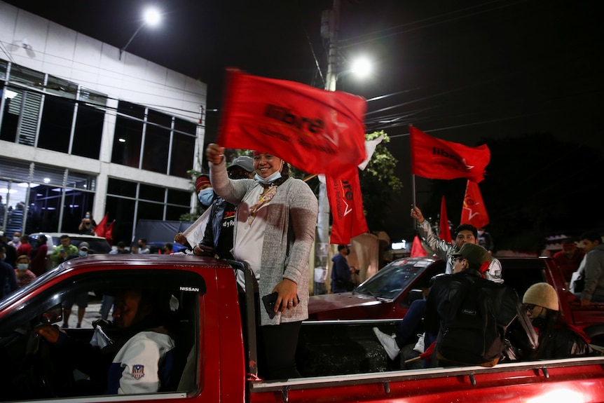 作为车队的一部分，Xiomara Castro 的支持者从汽车上挥舞着红色的自由旗帜