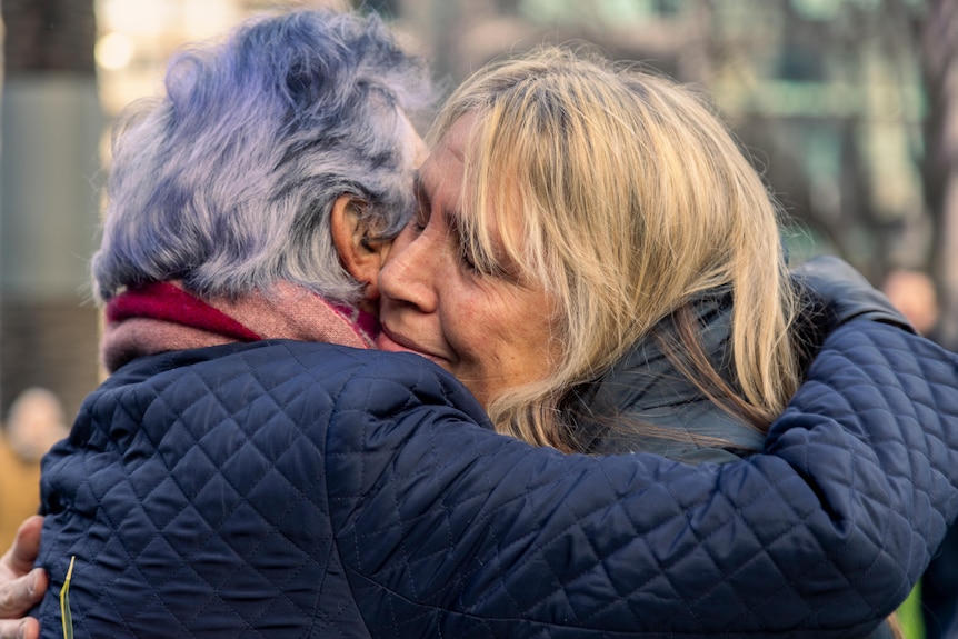 Two women embrace outside, dressed warmly on a winter morning.