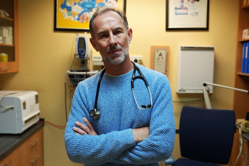 A man wearing a stethoscope crosses his arms and looks directly in to the camera.