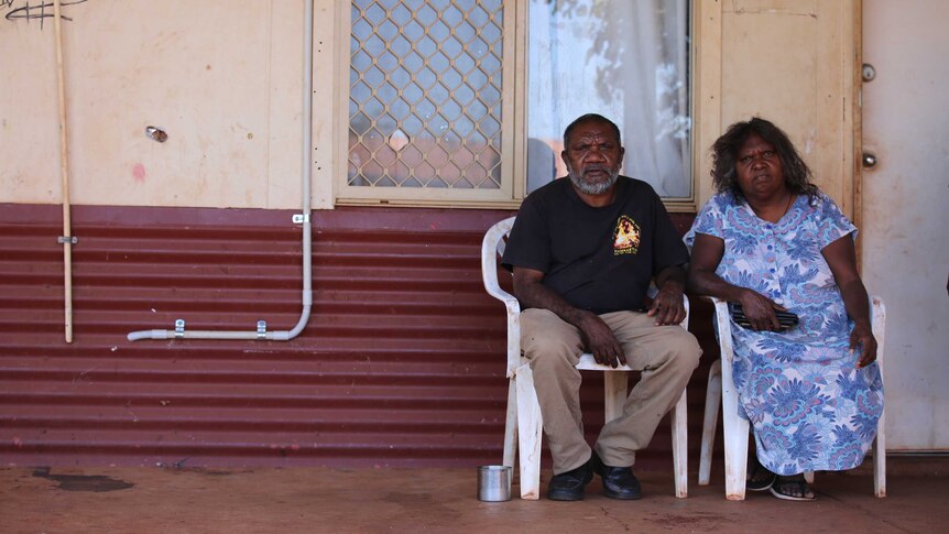 Aboriginal man sitting with his wife in front of their house.