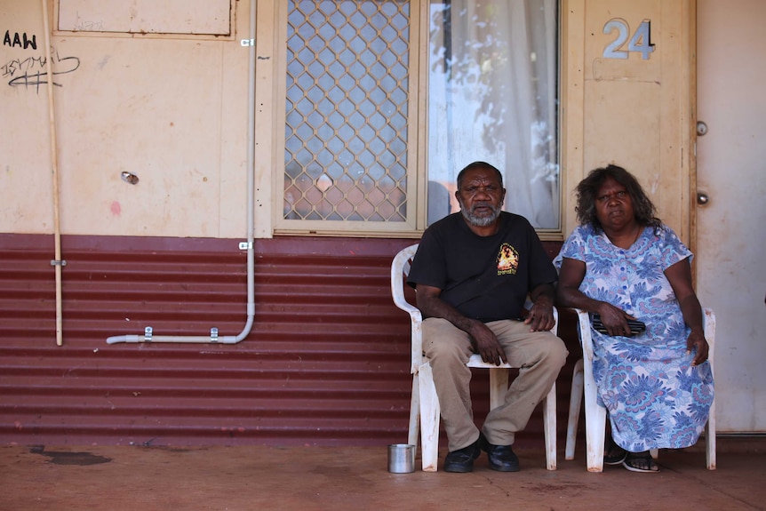 An Aboriginal man sitting with his wife in front of their house