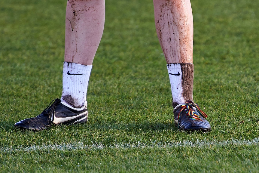 A pair of black sports boots with muddy white socks and a rainbow shoelace