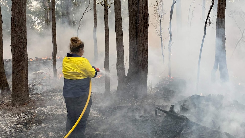 Woman in work uniform putting out a low-intensity fire with a hose.