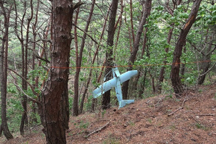 A crashed drone is seen in rugged bushland.