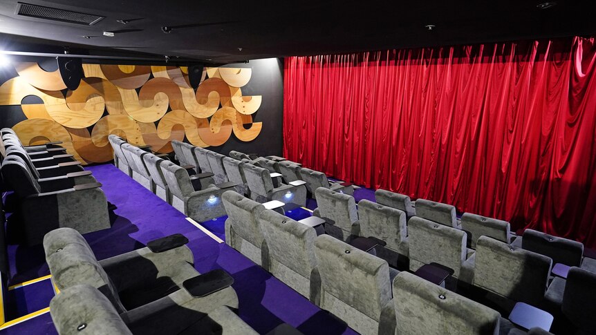 Empty chairs in a movie cinema with red curtains draped in front of the screen.