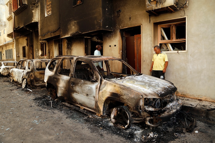 Men survey remains of burnt out cars on a street in Tripoli.