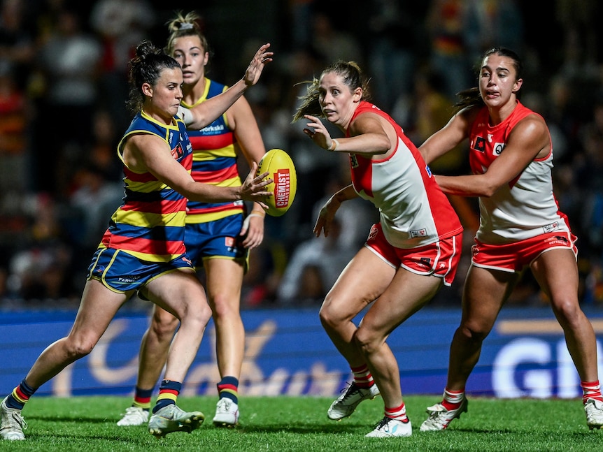 An Adelaide Crows AFLW player snaps a kick over a group of advancing Sydney Swans defenders towards goal.