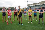 Eight football players wearing guernseys stand on an oval looking at the camera.