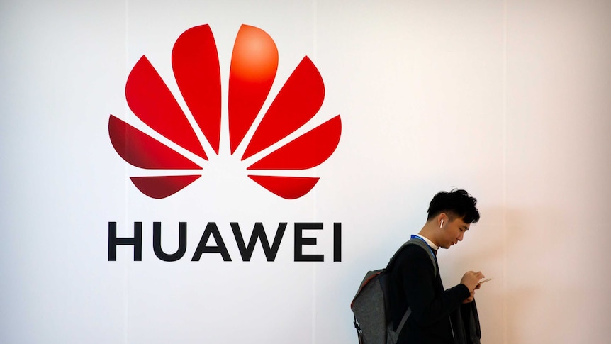 A man on looking down at his phone walks past a Huawei logo