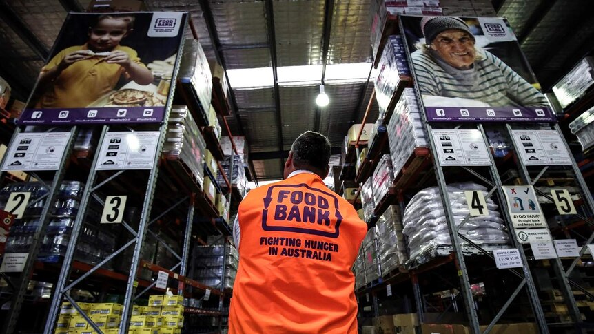 Michael Rose, CEO Foodbank Queensland, berdiri melihat barisan rak penyimpan makanan yang diselamatkan dari tempat pembuangan.