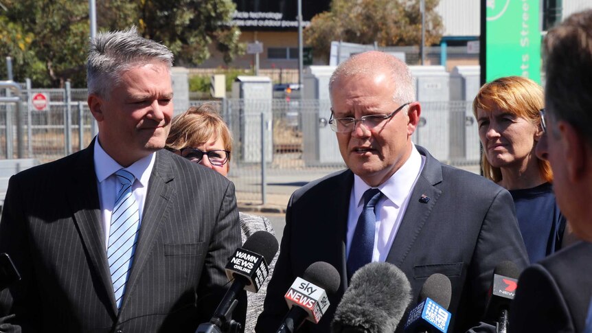 Scott Morrison and Mathias Cormann talk at a press conference in front of a train station.
