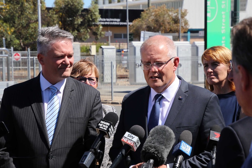Scott Morrison and Mathias Cormann talk at a press conference in front of a train station.