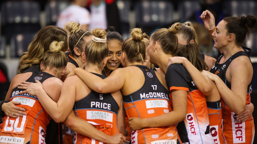 A group of Giants Super Netball players embrace in a circle as they celebrate beating the Swifts.