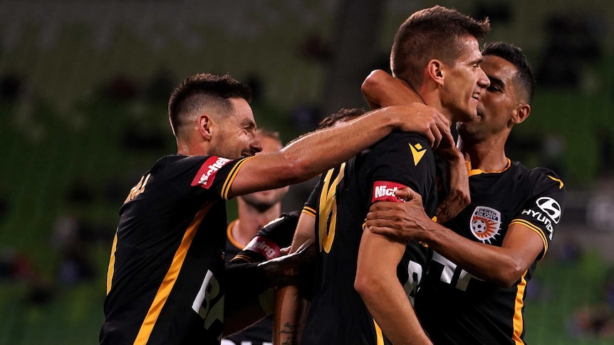 A group of footballers crowd around a teammate patting him on the back after he scores a goal.