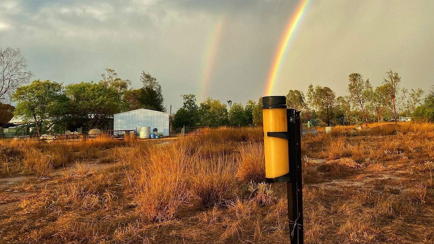 A rainbow grounds into a rain gauge beneath storm clouds