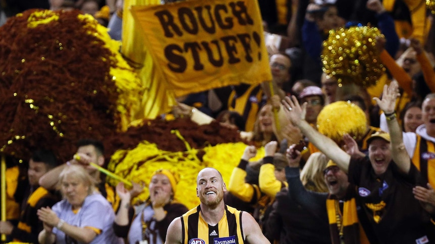 Jarryd Roughead smiles while standing in front of an adoring crowd. A fan's banner reads "ROUGH STUFF!".