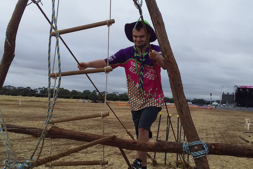 A man in a pink and purple scouts t shit on a ropes course. 